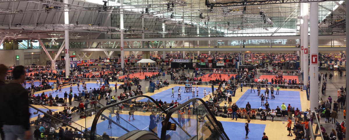 A convention hall filled with volleyball courts, teams and spectators at a Boston event